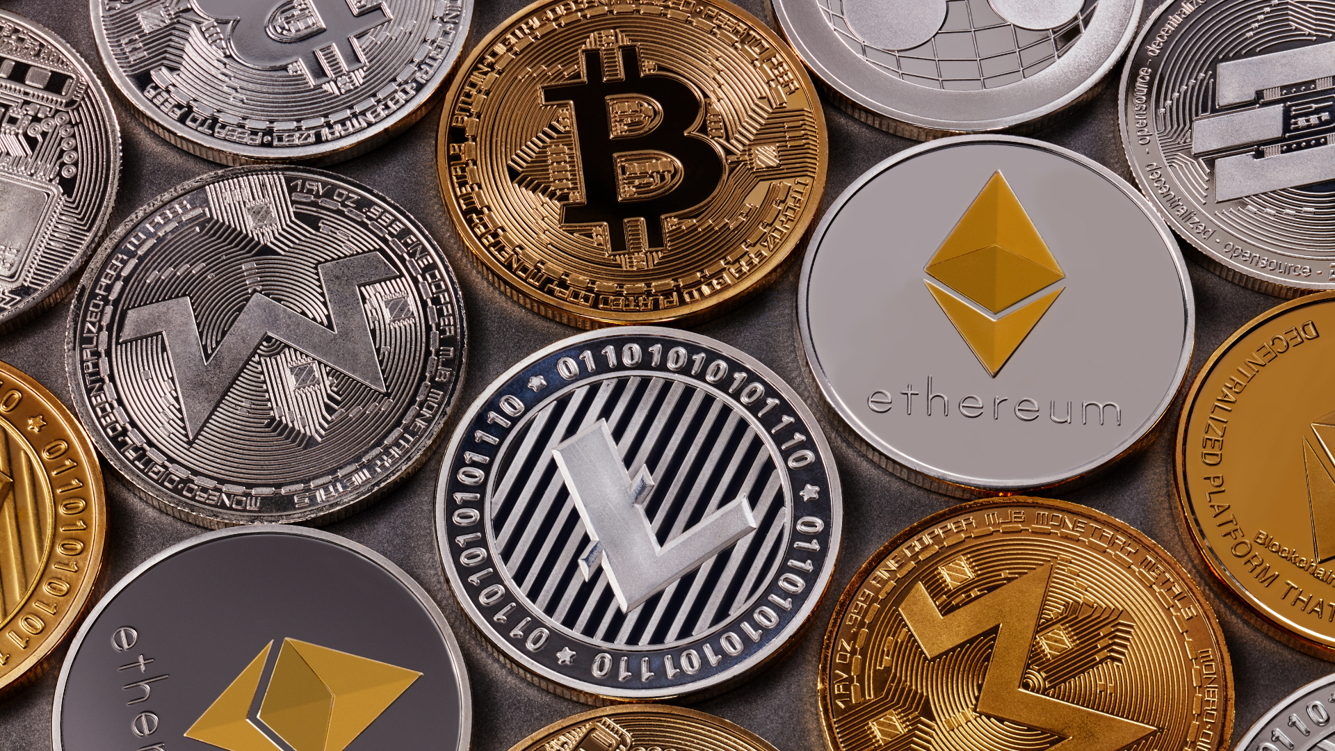 Verschiedene physische Darstellungen von Kryptomünzen, darunter Bitcoin, Ethereum, Litecoin und andere, dicht beieinander angeordnet.