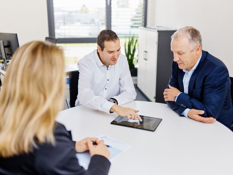 Eine Gruppe von Personen sitzt um einen Tisch herum und schaut in ein Tablet.