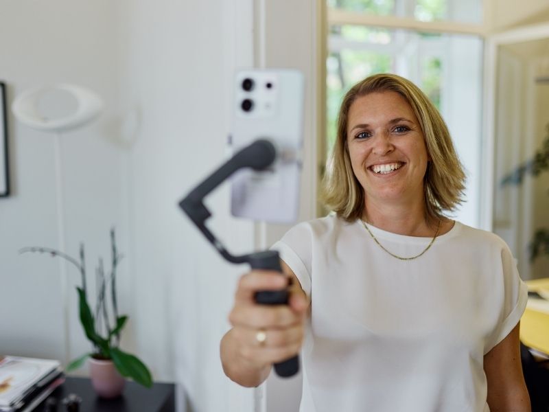 Eine Frau mit Handy und Stativ in der Hand.