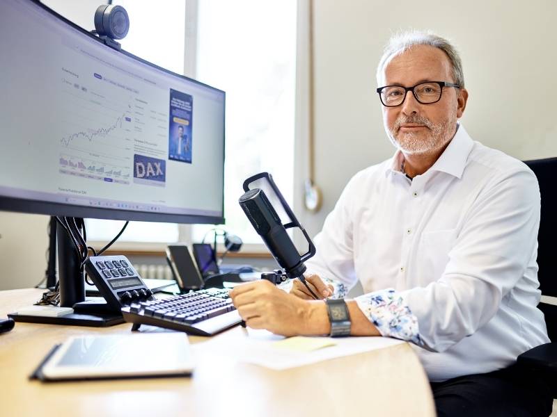 Ein Mann sitzt am Schreibtisch. Vor ihm steht ein Mikrofon und ein Computer.