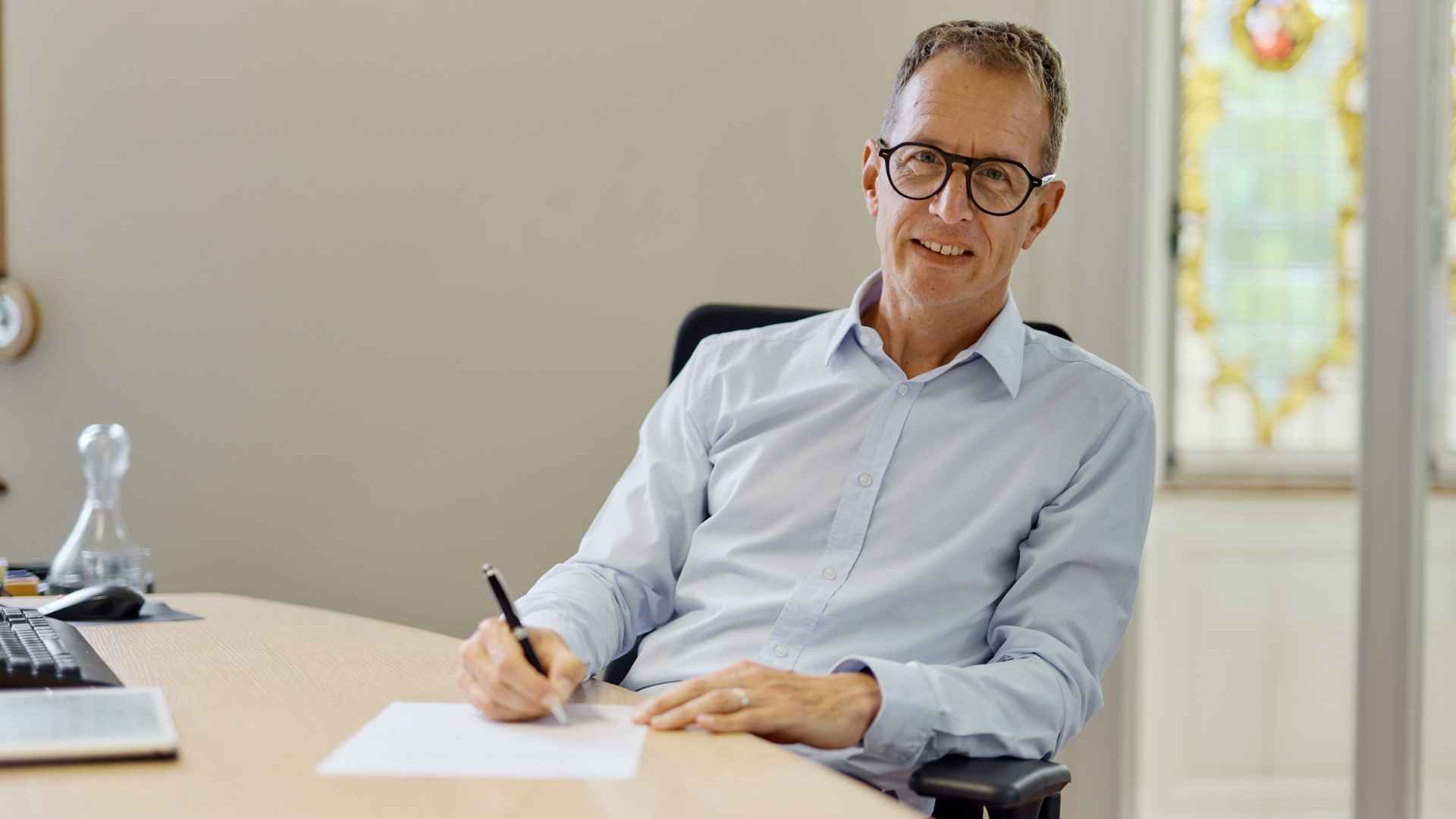 Ein Mann sitzt am Schreibtisch und schreibt etwas auf ein Blatt Papier.